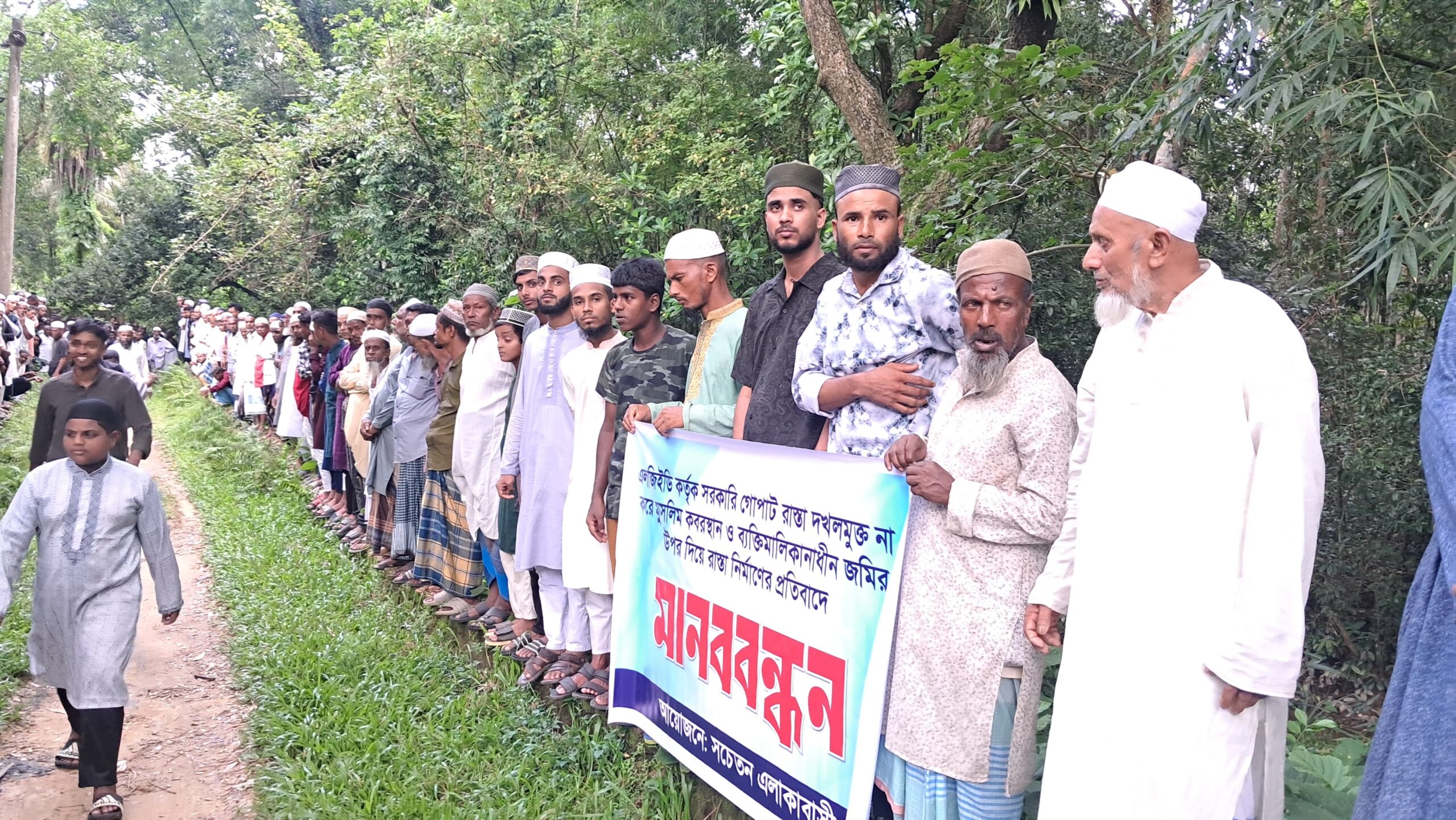 সরকারি জায়গা উদ্ধার না করে কবরস্থানের ওপর দিয়ে রাস্তা নির্মাণের প্রতিবাদে মানববন্ধ